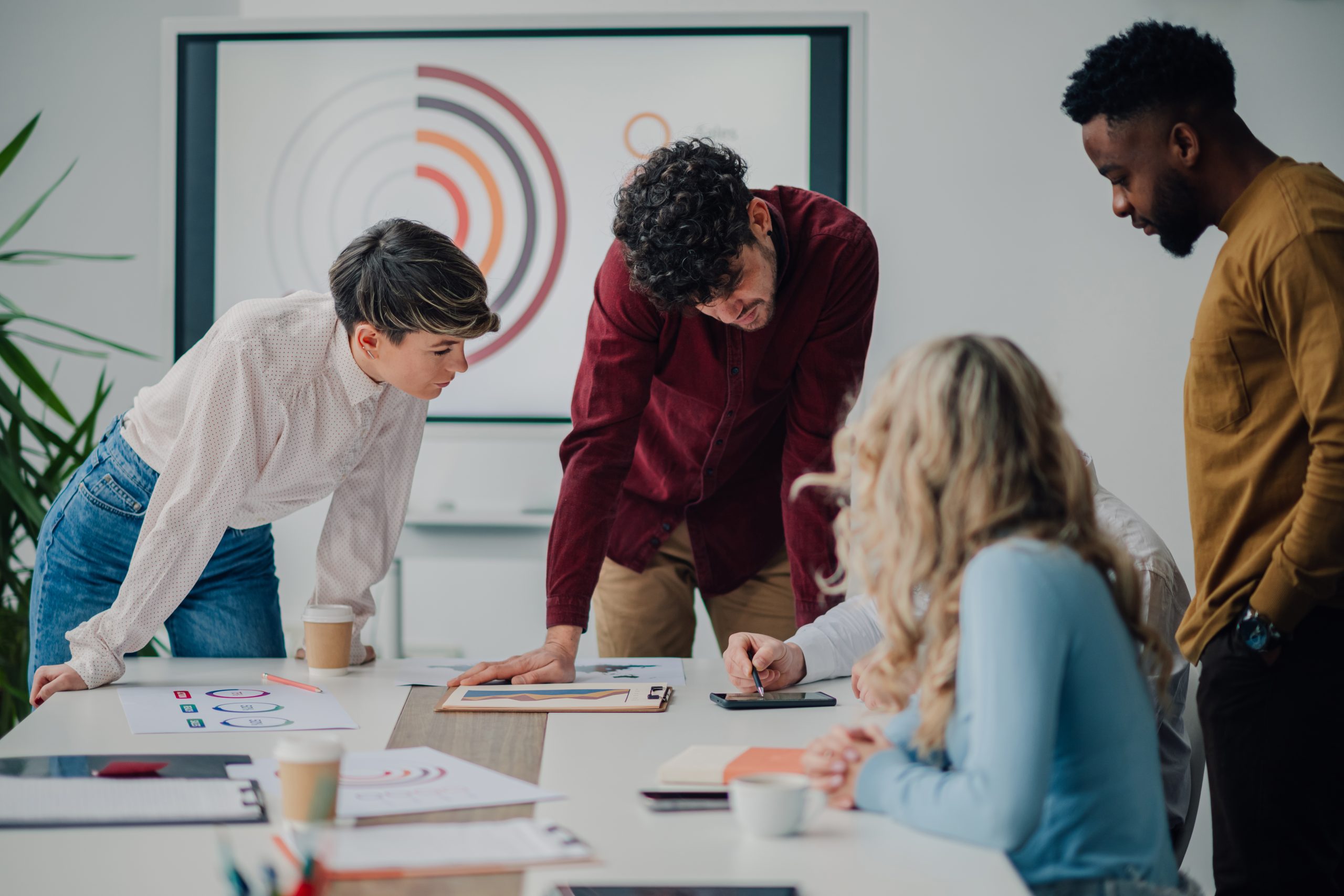 Diverse marketing team members are collaborating and strategizing, analyzing charts and reports on digital tablet, working together to achieve business goals during a productive office meeting